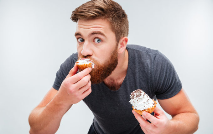 Close up portrait of a hungry bearded man biting cream cake isolated on white background