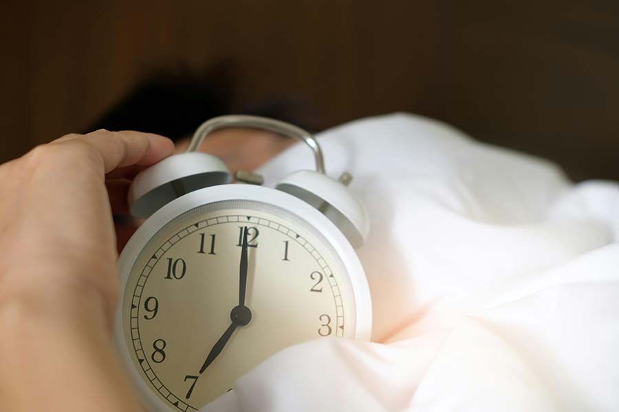 A hand turning off the alarm on a clock before an appointment with a sleep apnea dentist