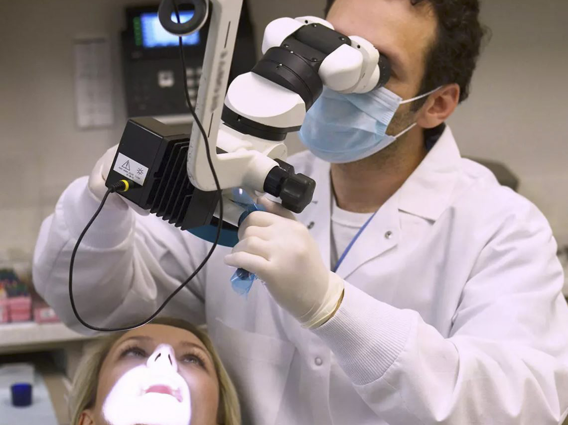 Endodontist at 209 NYC Dental performing emergency root canal treatment for a dental abscess using endodontic microscope.